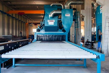 Continuous wheel blast machines with roller track